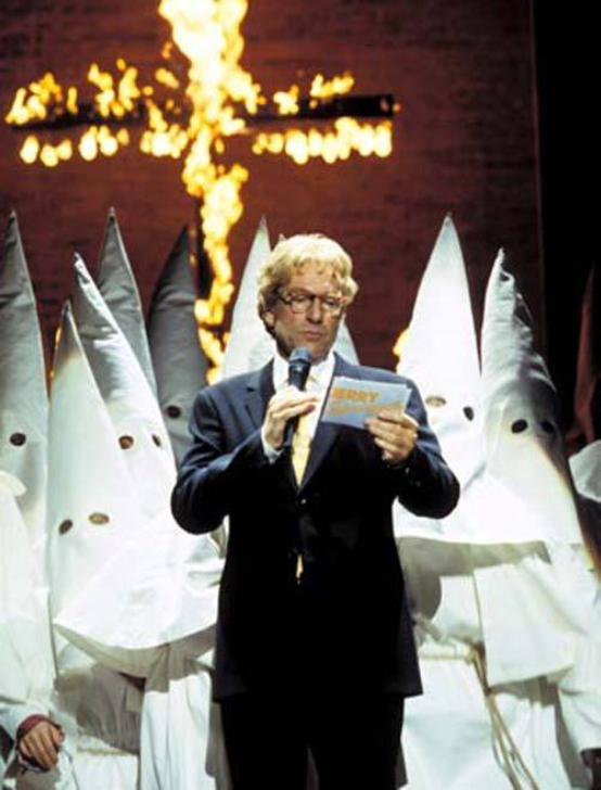 Jerry Springer the Opera A still from 'Jerry Springer The Opera'. A cross burns in the background as a man with blonde hair and glasses in a suit stands in front of a group of people in white pointy hoods and robes. The man holds a microphone and Jerry Springer cue cards.